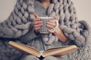 Combating seasonal depression: Woman sat with blanket, book and hot drink