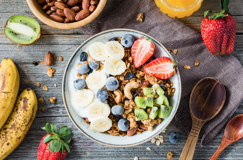 healthy bowl of granola, yoghurt and fruit surrounded by chopped fruit